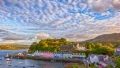 Colorful houses line a tranquil harbor under a vibrant sky, showcasing the charm of a small coastal village in the UK.