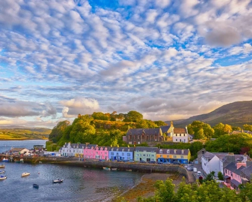 Colorful houses line a tranquil harbor under a vibrant sky, showcasing the charm of a small coastal village in the UK.
