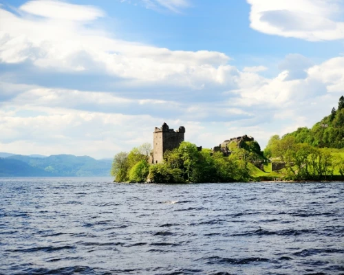 Scenic view of a castle on an island, surrounded by water and lush greenery, under a vibrant sky. Perfect for exploring UK history.