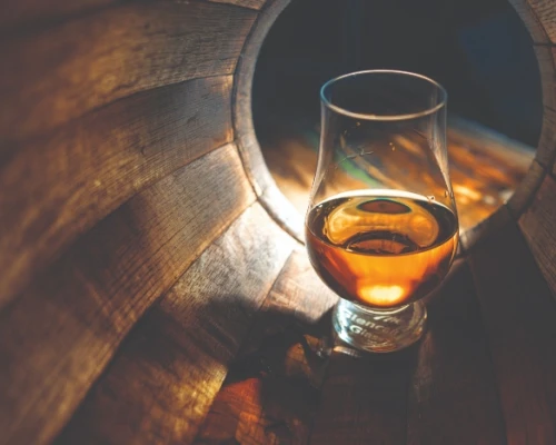 Glass of whiskey illuminated inside a wooden barrel, highlighting the rich amber color. Perfect for a cozy tasting experience.