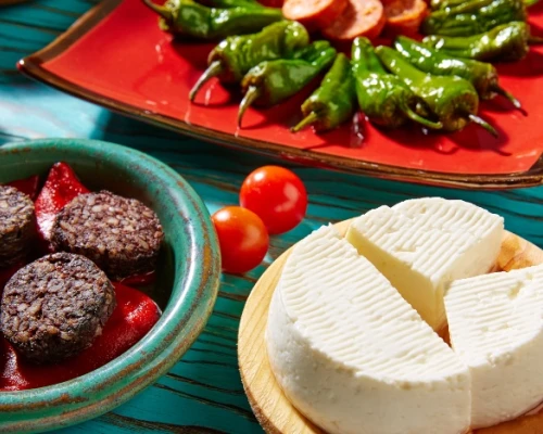An array of vibrant dishes featuring cheese, black pudding, cherry tomatoes, and green peppers on colorful plates.