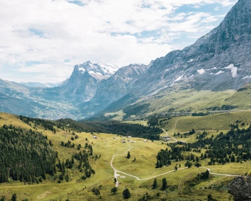 Lush green valley surrounded by majestic mountains under a partly cloudy sky, showcasing natural beauty perfect for exploration.