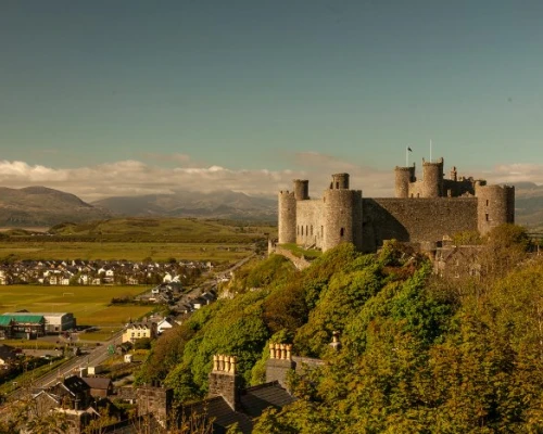 Historic castle perched on a hill, overlooking a scenic village and lush valleys under a clear blue sky.