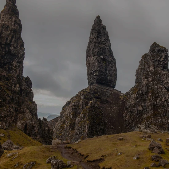Dramatic rock formations rise against a cloudy sky on a scenic landscape, showcasing the rugged beauty of the UK.